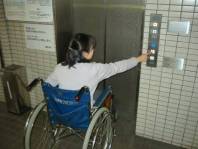 写真：エレベーター前でボタンを押す車いすの女性