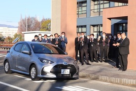 派遣職員が車で出発し、他の職員が並んで送り出している写真